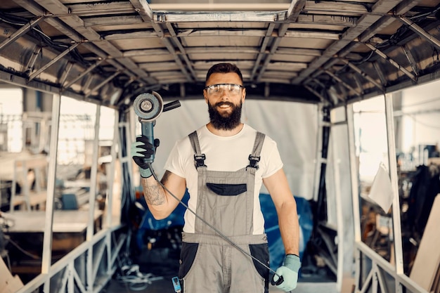 A happy mechanic standing in the middle of the bus with a grinder in hands