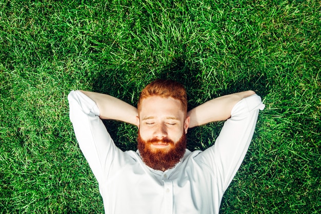 草の上に横たわっている幸せな男性。夏の日に赤ひげの美しいモデル。