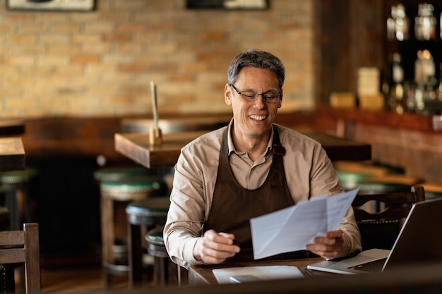 Happy mid adult barista going through reports while working in a bar.