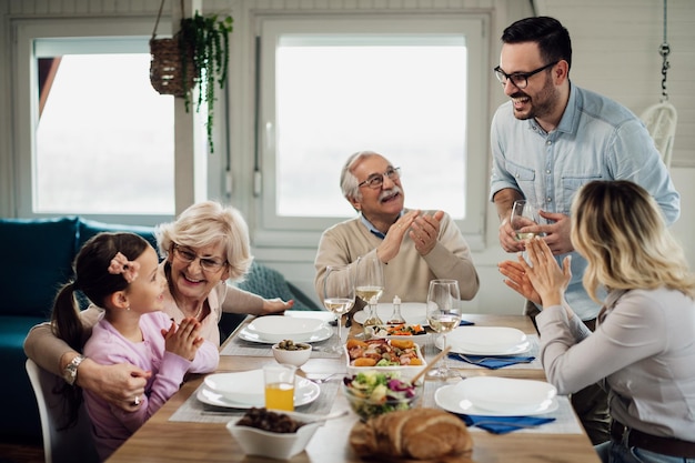 Happy mid adult man holding a proposing a toast during lunch while his family is applauding him