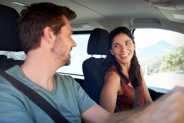 お互いに笑顔で車で運転している幸せなミッドアダルト白人カップルのクローズアップ側面図