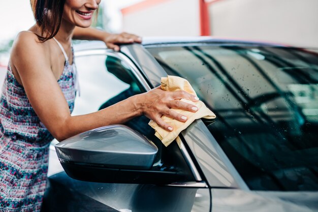 Happy middle age woman washing car in the evening at car wash station.