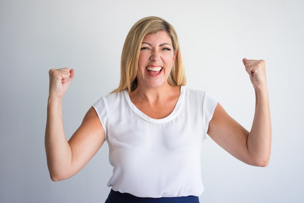 Happy middle aged Caucasian woman raising fists in winning gesture 