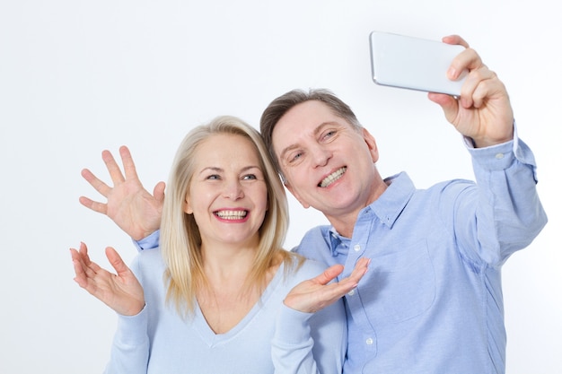 Felice coppia di mezza età tenendo selfie con lo smartphone isolato su bianco
