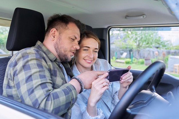 Happy middle aged couple using smartphone together sitting in the car