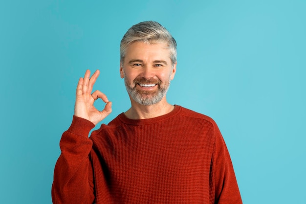 Happy middle aged man showing okay gesture on blue