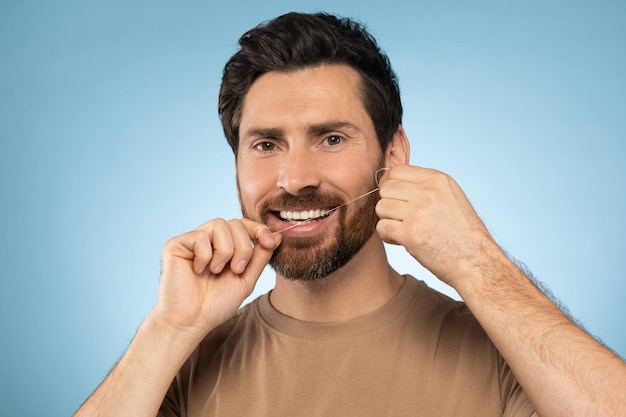 Happy middle aged man using dental thread floss and smiling cleaning teeth after food posing over blue background