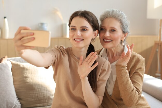 Happy middle aged mother and daughter taking selfie at home.