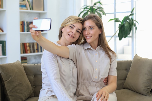 Photo happy middle aged mother and daughter taking selfie at home.