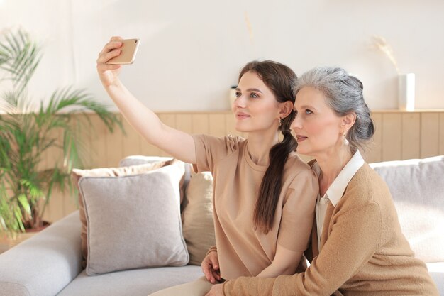 Happy middle aged mother and daughter taking selfie at home.