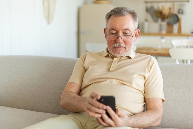 Happy middle aged senior man holding using smartphone touch screen typing scroll page stylish older