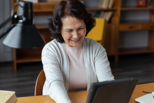 Happy middle aged senior woman holding tablet talk on video call with friends family Laughing mature old senior grandmother having fun talking speaking with grown up children online