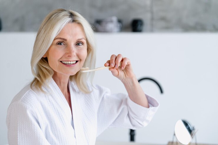 Happy middle aged woman hold bamboo toothbrush and clean teeth
