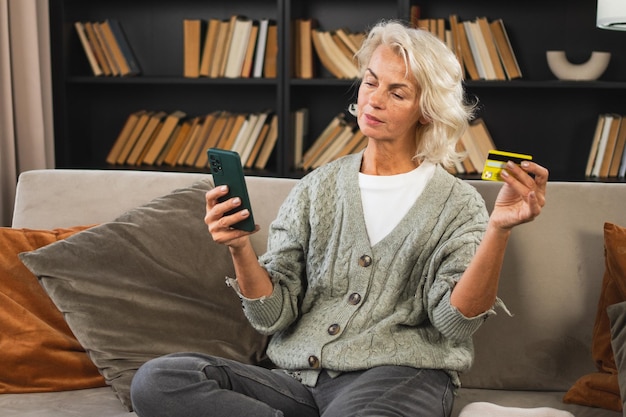 Happy middle aged woman shopping online with smartphone paying with credit card mature lady buying