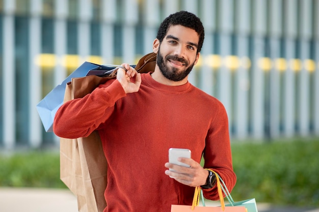 Happy middle eastern man holding smartphone shopping in app outside