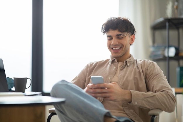 Happy middle eastern man using mobile phone sitting at home