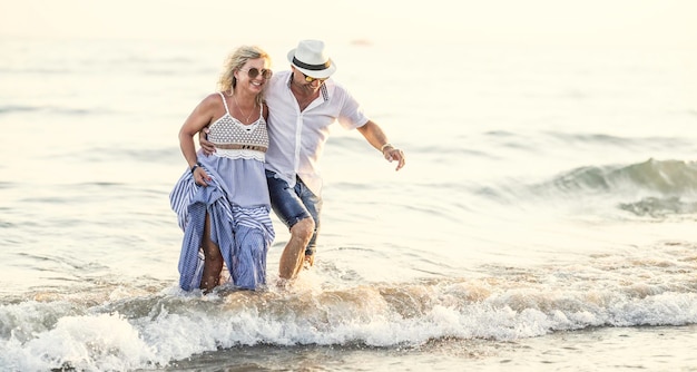 Happy middleaged couple in love walking in the water on the beach at sunset