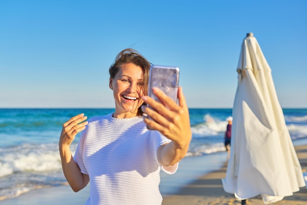 Happy middleaged woman talking on smartphone using video call on beach