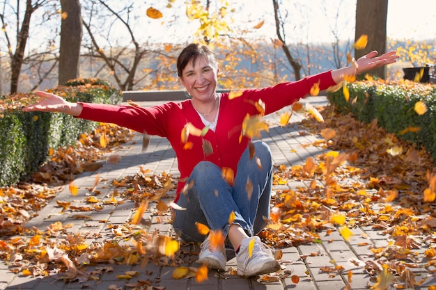 행복한 중년 여성은 가을 공원에서 노란 잎을 던졌습니다