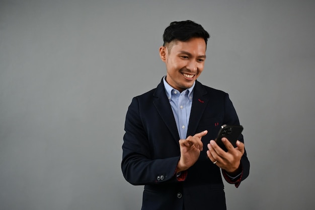 Happy millennial Asian businessman using his smartphone isolated gray background