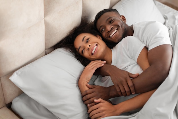 Photo happy millennial black couple flirting and embracing on comfortable bed