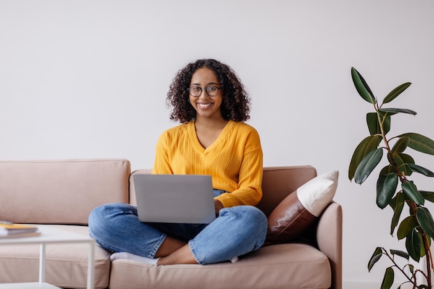 Photo happy millennial black woman in glasses using laptop computer sitting on couch at home copy space
