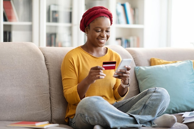 Happy millennial black woman using smartphone and credit card