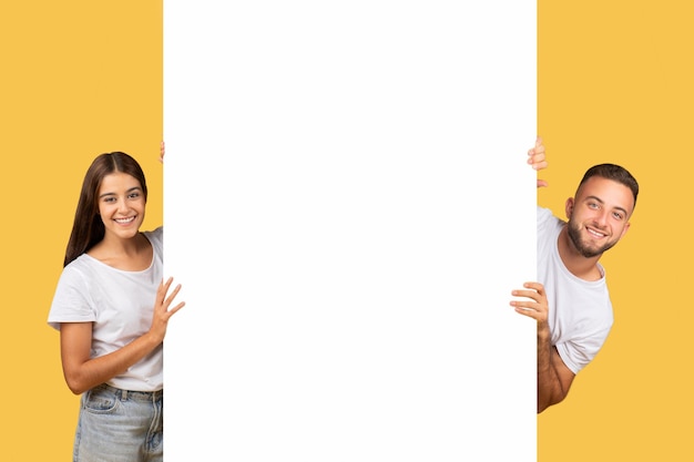 Photo happy millennial european couple in white tshirts with big banner with empty space