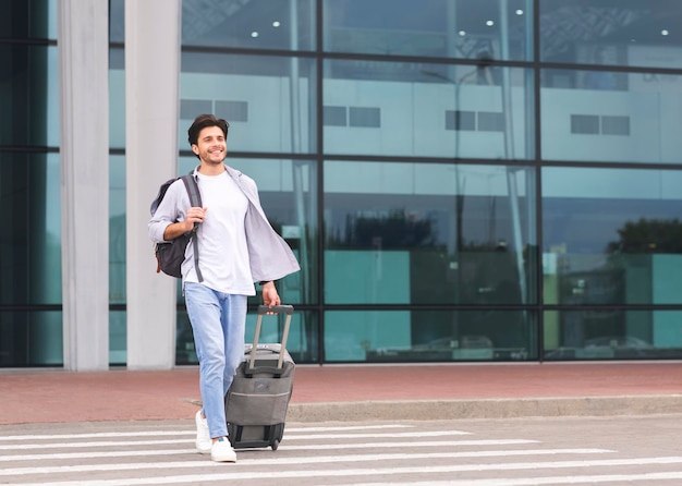 Happy millennial guy going out of airport building