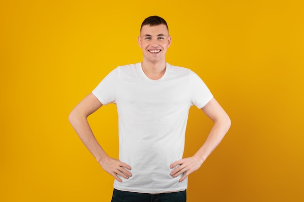 Happy millennial man posing holding hands on hips yellow background