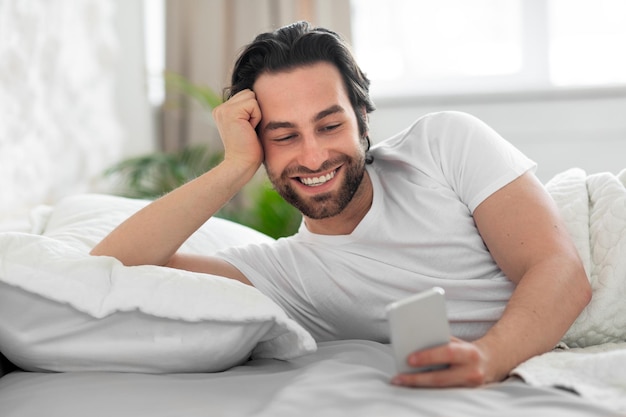 Happy millennial man using cell phone after waking up