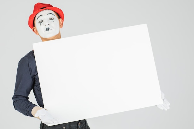 Happy mime artist holding a blank white board on a white\
background