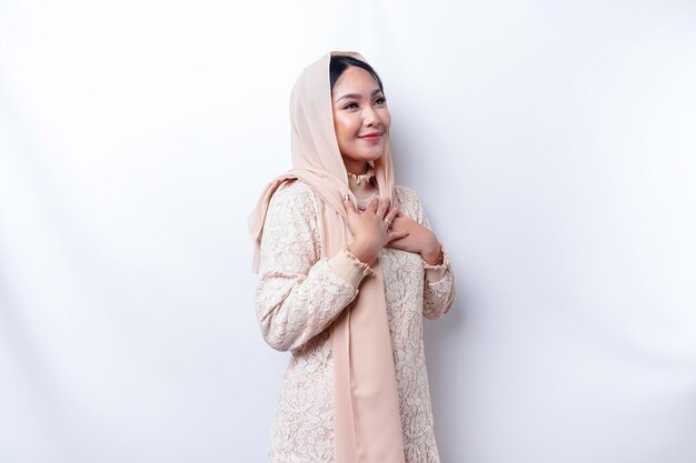 Happy mindful thankful young Asian Muslim woman with her hand on her chest smiling isolated on white background