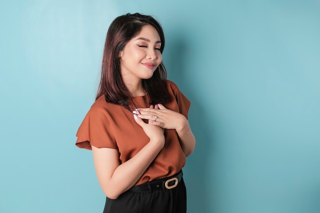 Happy mindful thankful young woman hand on chest smiling isolated on blue background