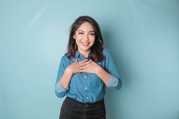 Happy mindful thankful young woman holding hands on chest smiling isolated on blue background feeling no stress gratitude mental health balance peace of mind concept