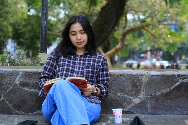 公園の教育コンセプトで本を読んで幸せなマインドフルな若いアジア人女性大学生