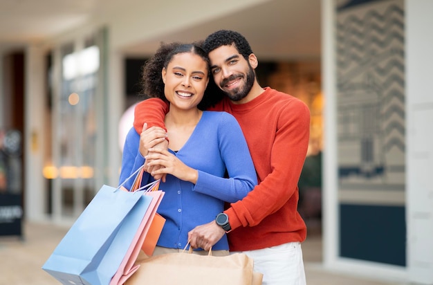 Happy Mixed Couple Shopping Posing With Shopper Bags Hugging Outside