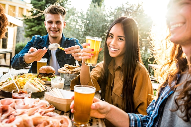 屋外で一緒に夕食をとる幸せな混血家族-テラスでビールを飲みながらおしゃべりを楽しんでいる若者-裏庭のホームパーティーを祝う多文化の友人-友情の概念