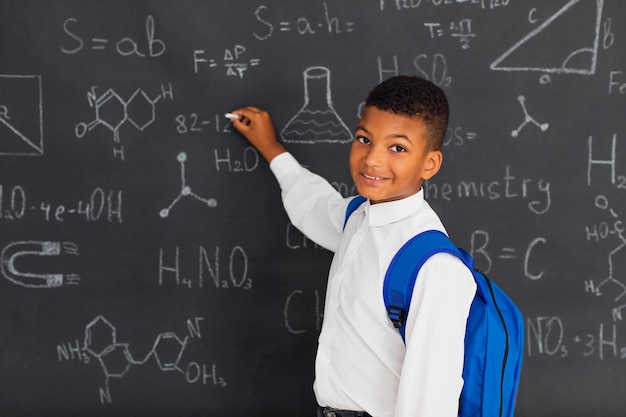 Happy mixed race schoolboy solving problems near the blackboard at school back to school concept