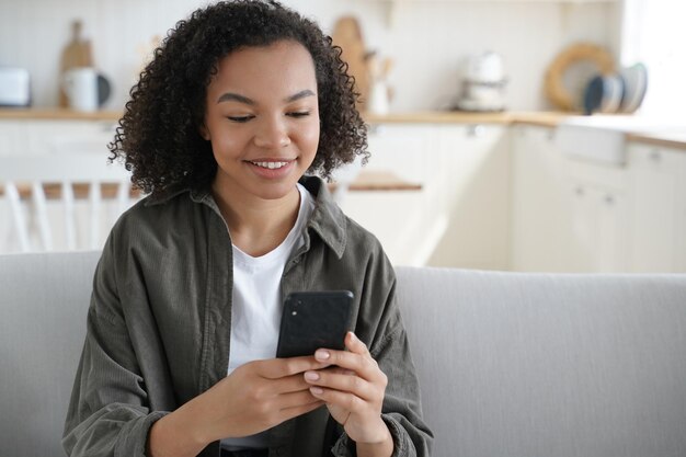 Happy mixed race teen girl holding smartphone uses mobile apps chatting or shopping online at home