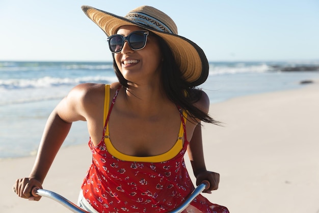Счастливая женщина смешанной расы, весело проводящая время на пляжном отдыхе на велосипеде. время отдыха на свежем воздухе у моря.