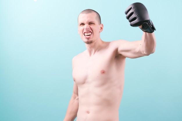 A happy mma fighter in black gloves rising his fist up on a\
blue background celebration strength training boxing sport fight\
fitness strong male punch black mma athletic battle