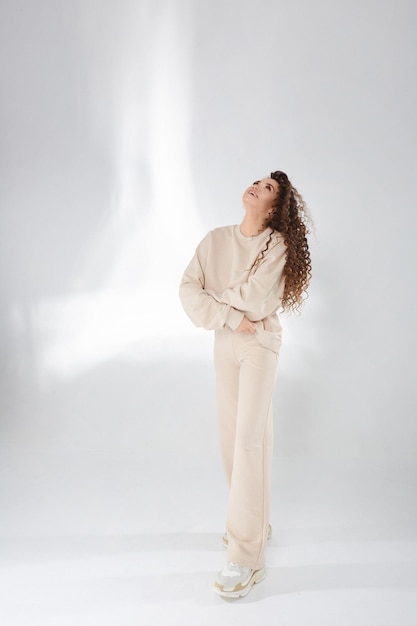 Happy model girl with afro hairstyle in a trendy sweatshirt posing with folded hands, laughing and looking up on the white background.