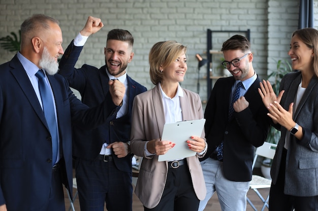 Фото Счастливые современные деловые люди держат руки поднятыми и выражают радость, стоя в офисе.