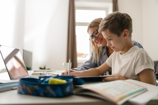 写真 幸せな母親と息子が一緒に宿題をしたり、ラップトップで勉強したりする家庭教育