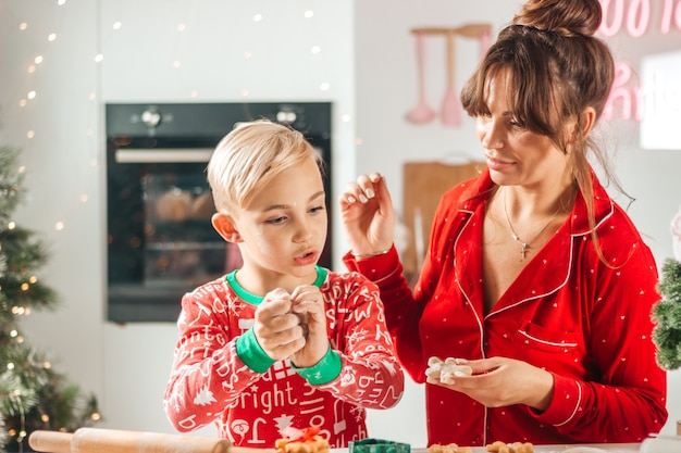 Happy mom and baby in red pajamas in the kitchen looking at the camera for christmas