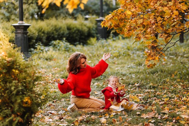 Happy mom and child are walking and having fun playing with autumn leaves in the fall park outdoors