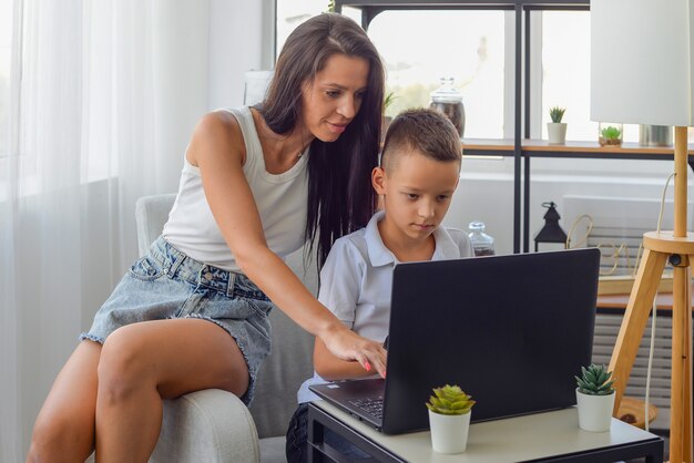 一緒にコンピュータの家族で宿題をしている幸せなママと子供