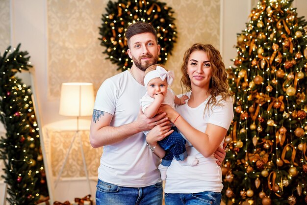 Happy mom and dad standing near Christmas tree in living room while holding little cute baby girl