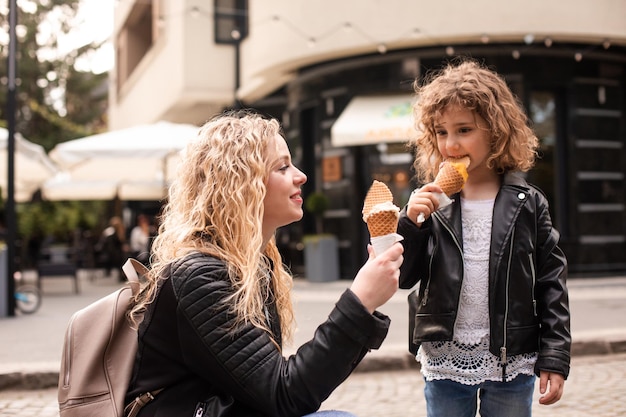 The happy mom and daughter are holding ice cream while walking